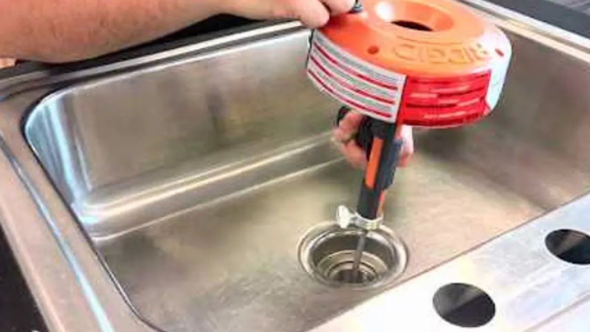 Plumber using a drain auger to clear a clogged kitchen sink drain in Sun City, AZ